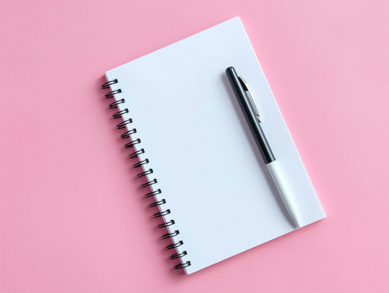 A spiral notebook and pen on a plain coloured surface